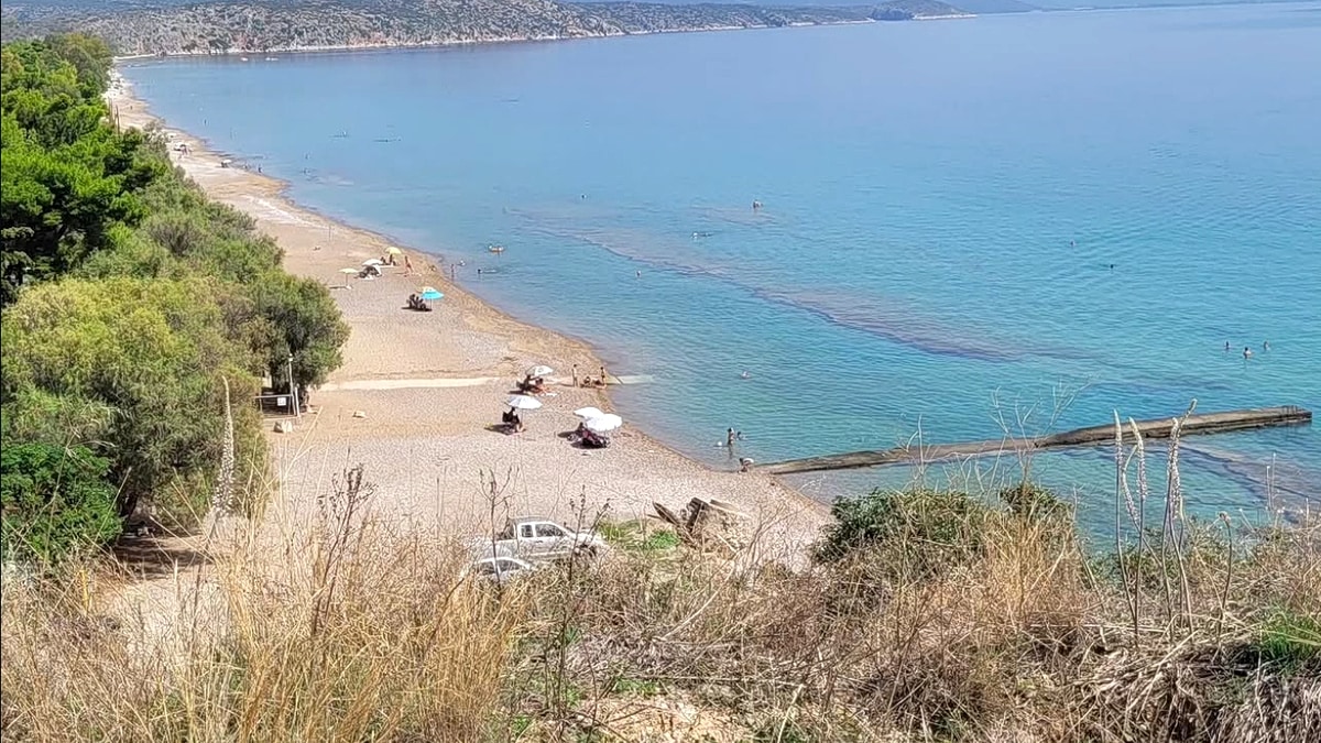 Tolo Beach in Nafplio, looking down the long sandy crescent with sunbeds and umbrellas along the shore and the headland of the bay behind